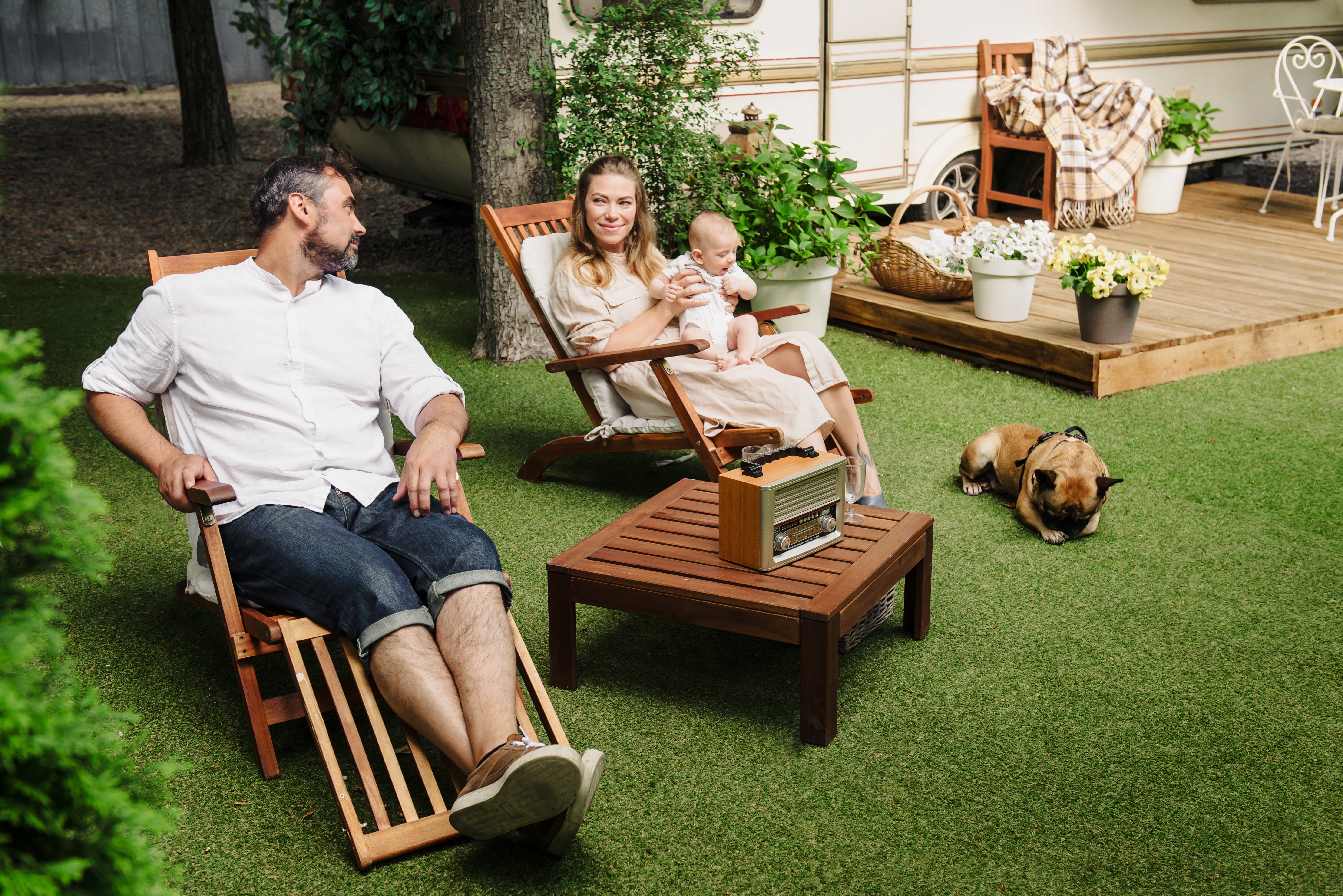 family-with-baby-dog-spending-happy-time-together-near-trailer-outside-deck-chair-traveling-lifestyle-with-camper