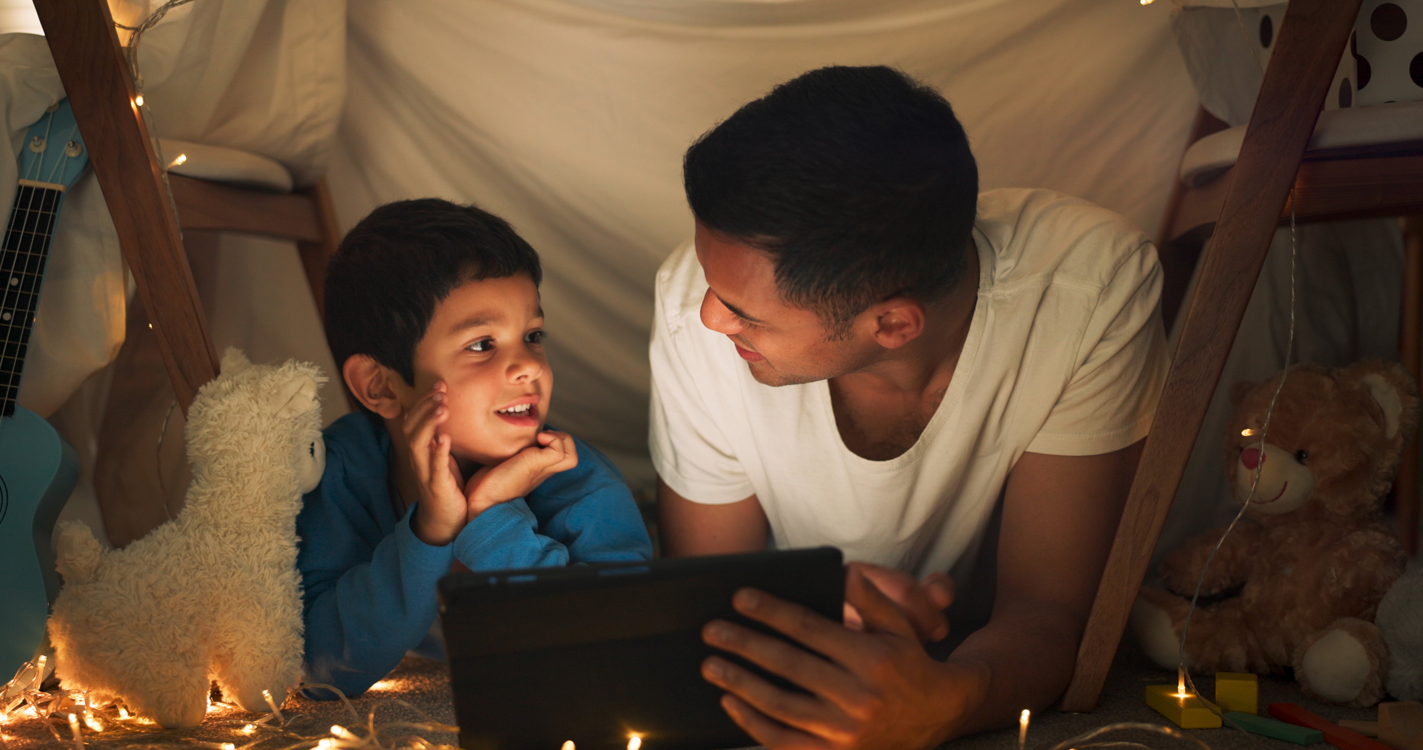 night-father-son-with-tablet-movie-with-streaming-blanket-tent-sleepover-with-bonding-fairy-lights-happy-evening-dad-child-with-technology-pajamas-relax-with-cartoon-fun